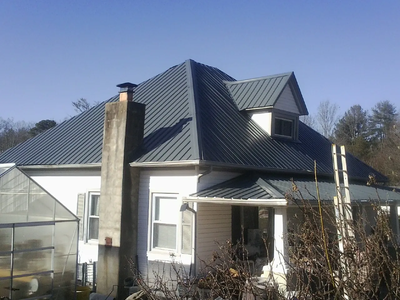 Dark blue standing seam metal roof on a white farmhouse with dormer — Slate & Tile Roof Repair by Roofing Brothers in Creighton