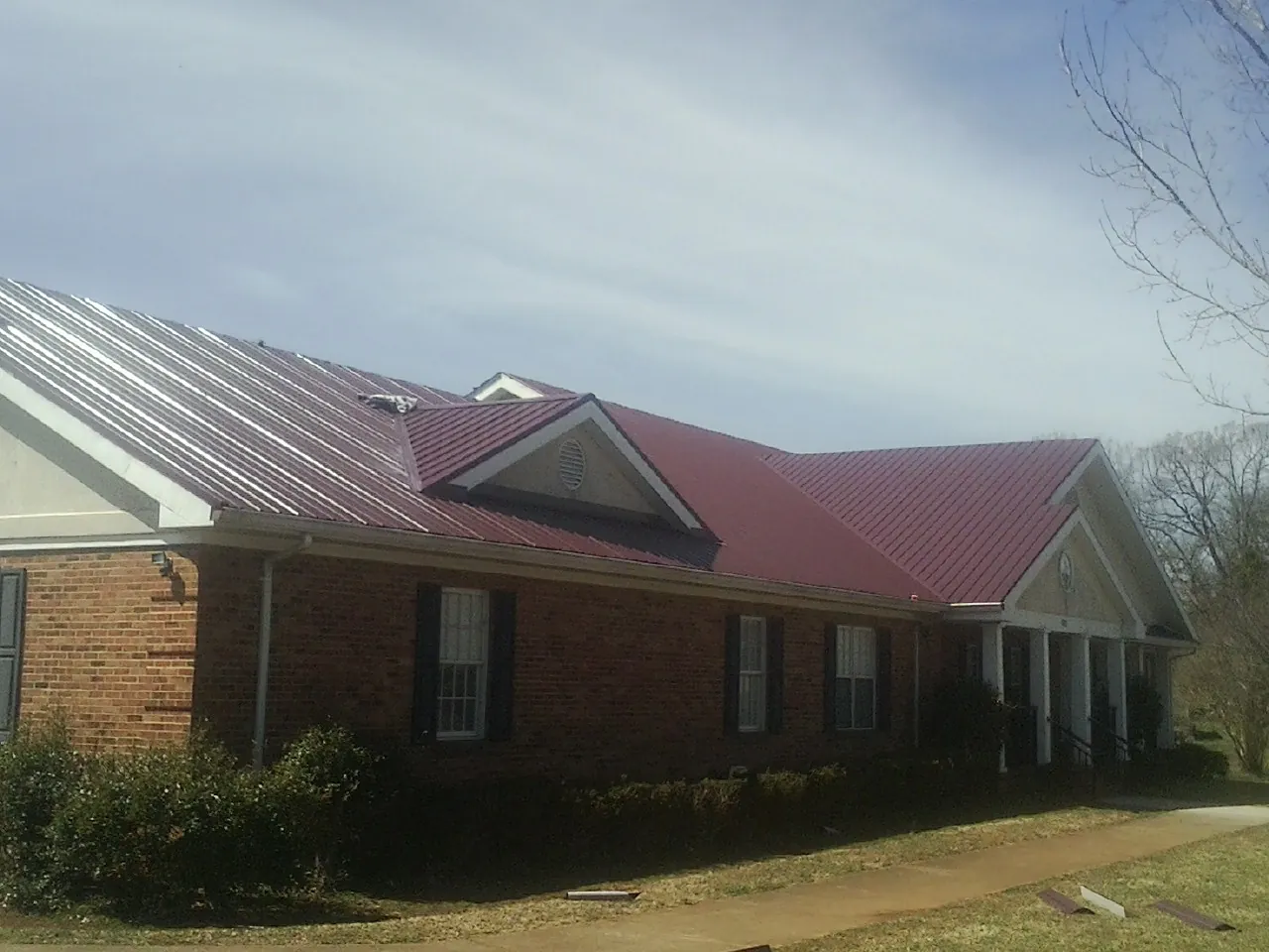 Red metal roof with gabled entries on a long brick building, from a Hail Damage Roof Repair job in Creighton
