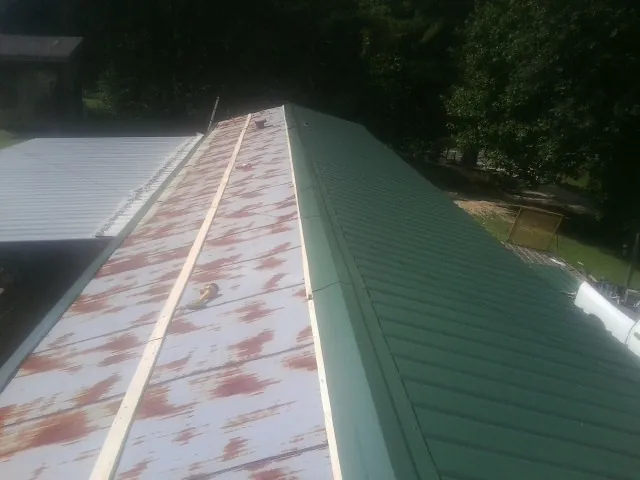 Old rusted panels beside newly installed green metal roofing in Creighton