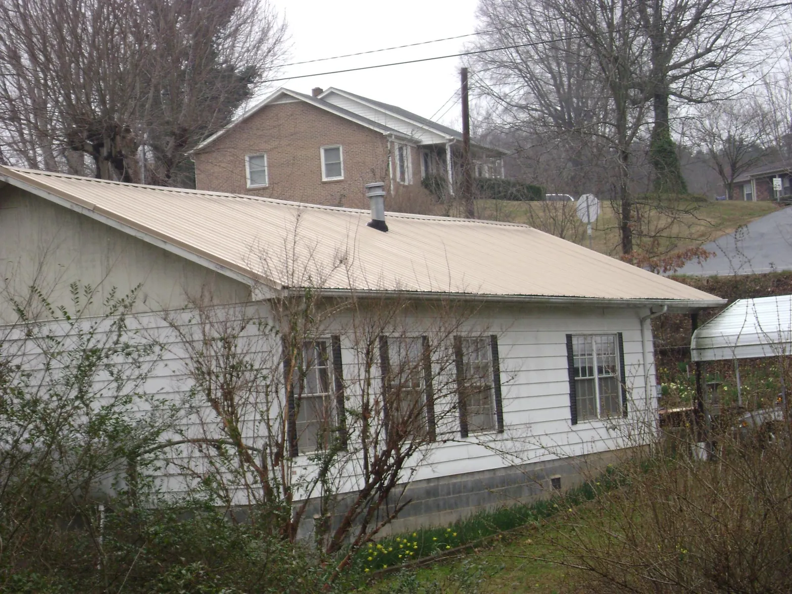 Tan metal roof on a white sided house set into a hillside — Commercial Roofing by Roofing Brothers in Creighton