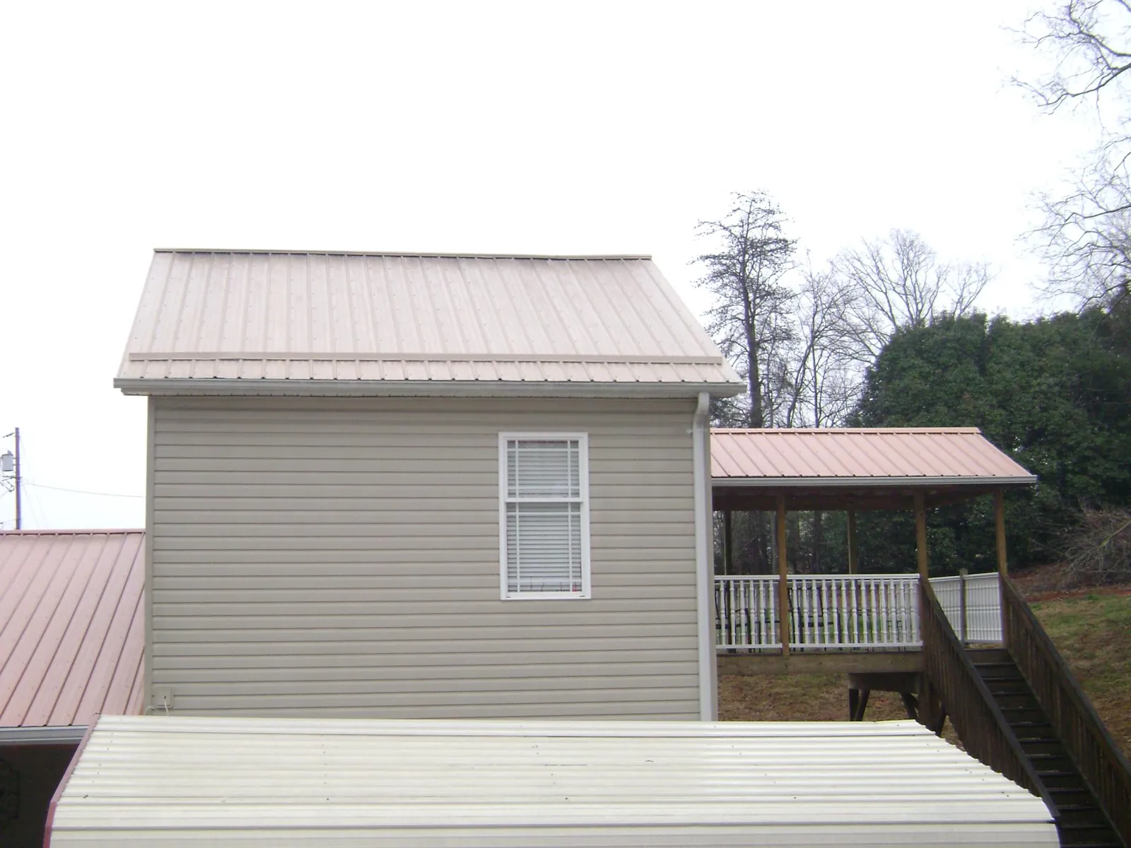 Tan metal roofs on a two story addition and attached porch, from a Roof Replacement job in Creighton
